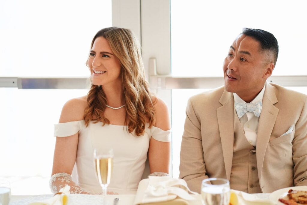 Bride and groom sitting at head table smiling off to the left at a guests speech