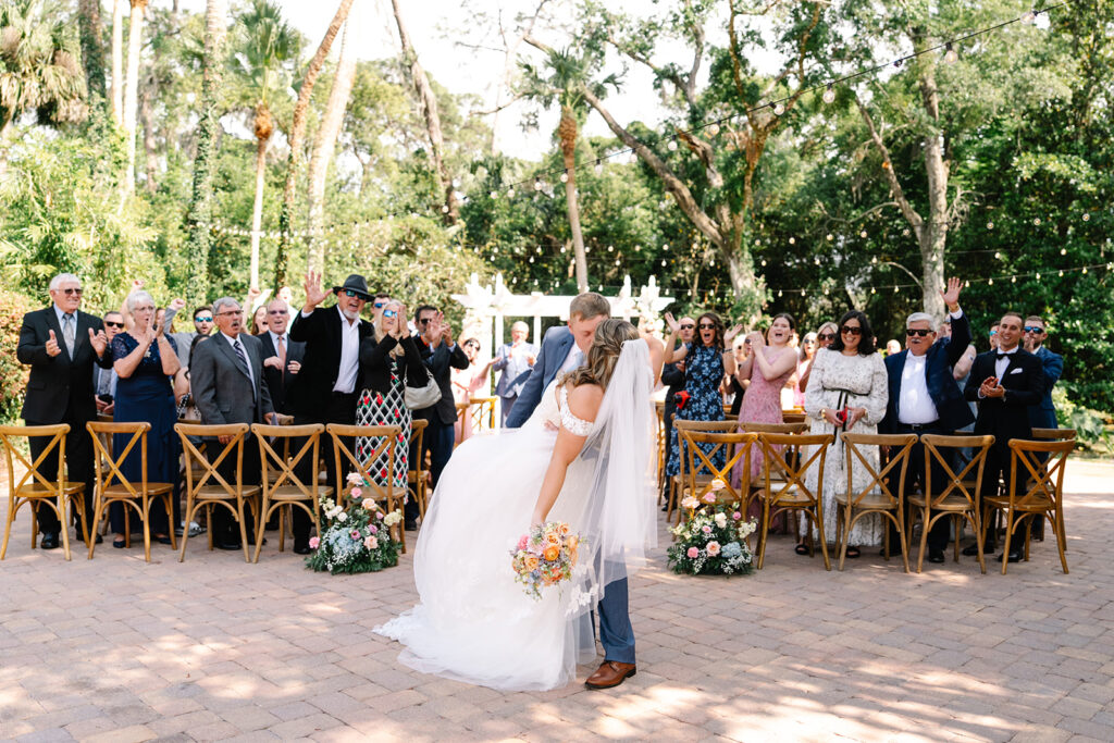 Bride and groom kissing while the groom dips the bride at the end of walking back down the aisle after getting married.