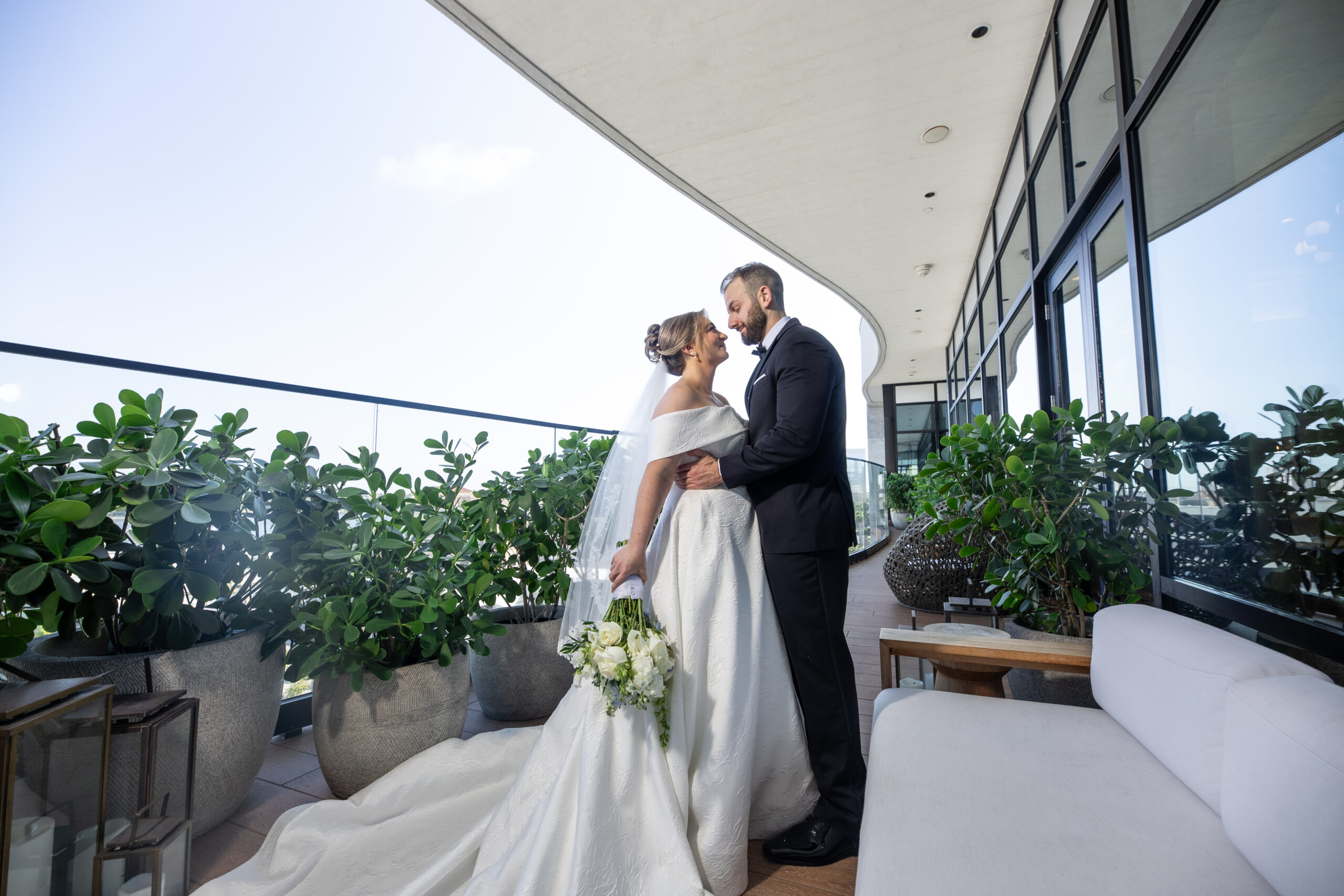 Groom holding the bride as they look lovingly into each others eyes standing in front of a lush greenery patio space