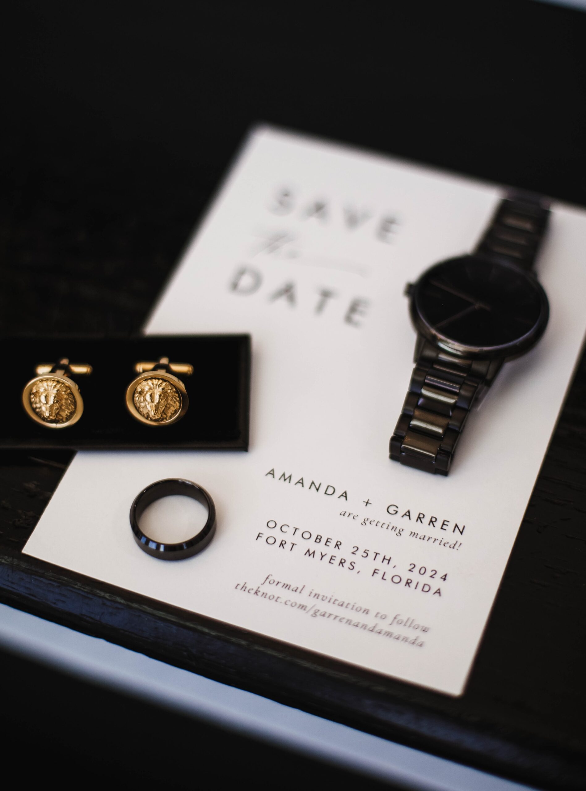 Stylized flat lay of the groom’s black watch, wedding band, gold lion cufflinks, and Save the Date card for Amanda and Garren’s Fort Myers wedding.
