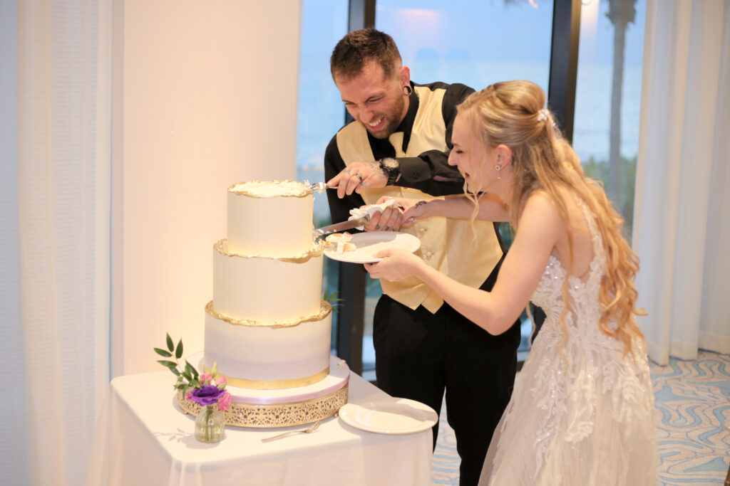 Joyful couple cutting their three-tier white and gold wedding cake, capturing a classic cake-cutting moment.