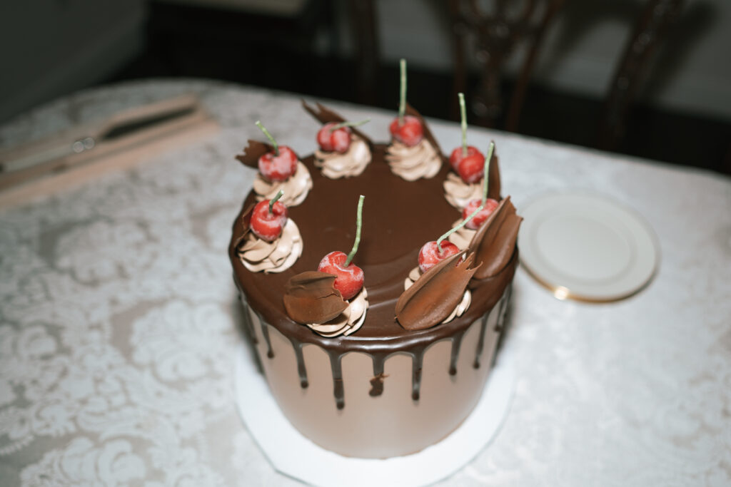 Elegant chocolate cake topped with cherries and frosting swirls, a modern option in the wedding cake vs dessert table debate.