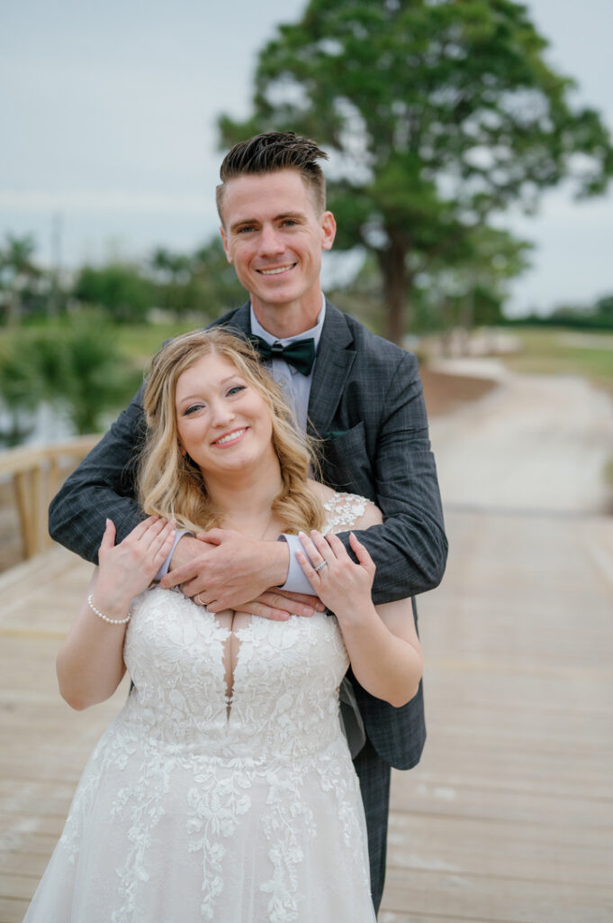 Bride and groom embracing on a wooden walkway surrounded by greenery at their Florida wedding celebration.