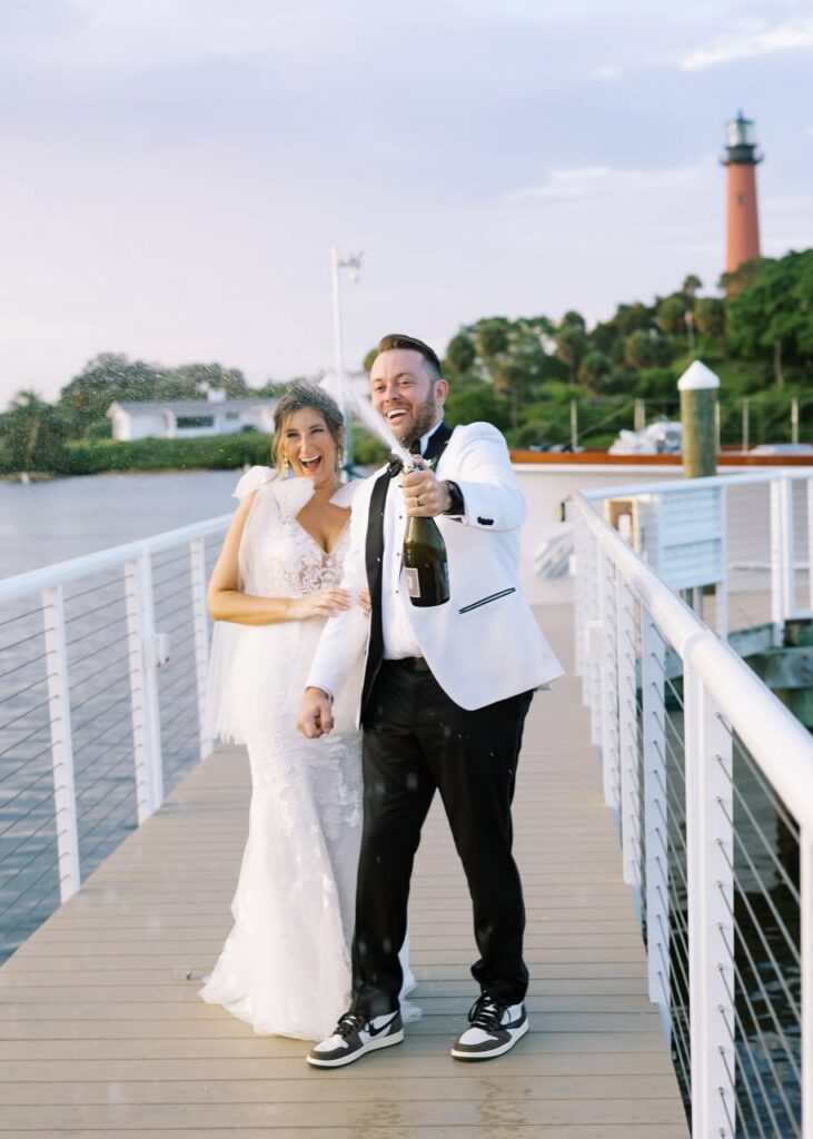 couple popping champagne on a doc by the water